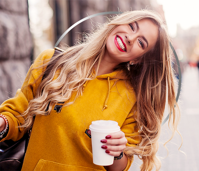 Happy young woman in yellow hoodie holding paper coffee cup